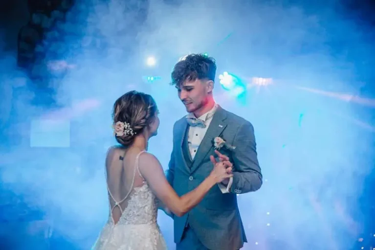 Brautpaar beim ersten Tanz, umgeben von Nebel und farbigen Lichtern, romantische Hochzeitsatmosphäre.