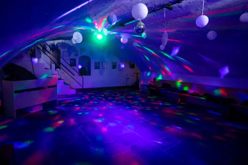 Keller-Partyraum mit bunter Disco-Beleuchtung und hängender Dekoration in dunkler Atmosphäre.