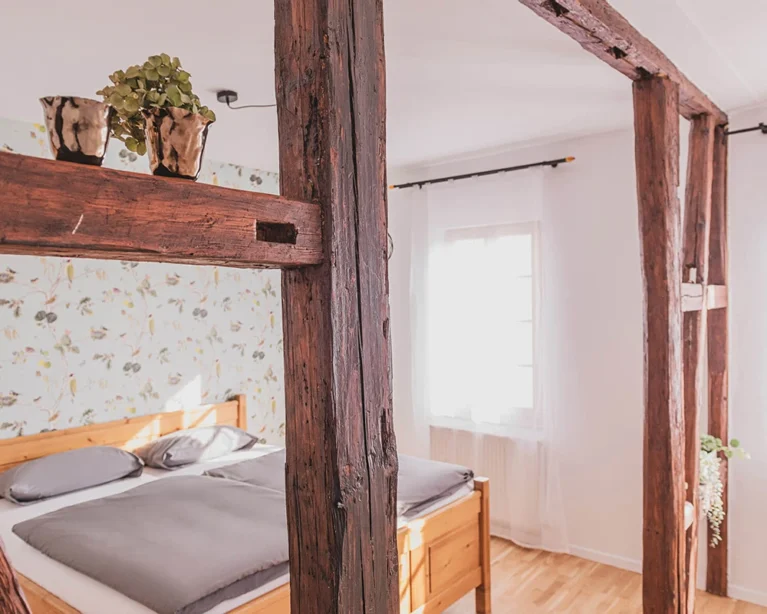 Gemütliches Schlafzimmer mit rustikalen Holzbalken, modernem Doppelbett und dekorativer Tapete im Landhausstil.