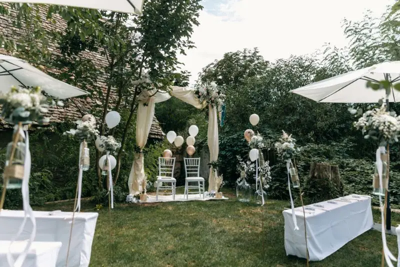 Gartenhochzeit Setup mit Blumen, Luftballons, Stühlen und Pavillon unter freiem Himmel im Grünen.